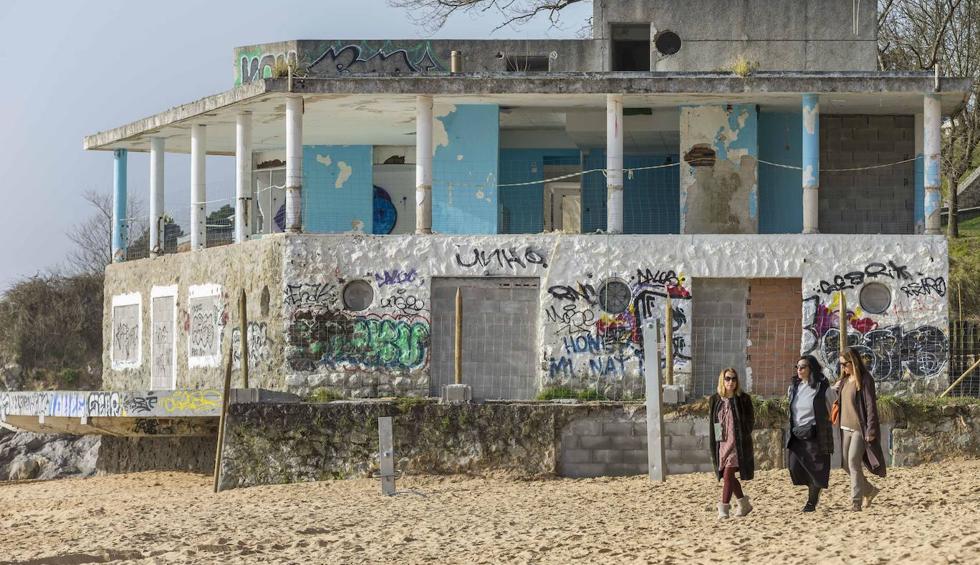 Tres mujeres pasean por la playa por delante del edificio de La Horadada, vallado en su perímetro.