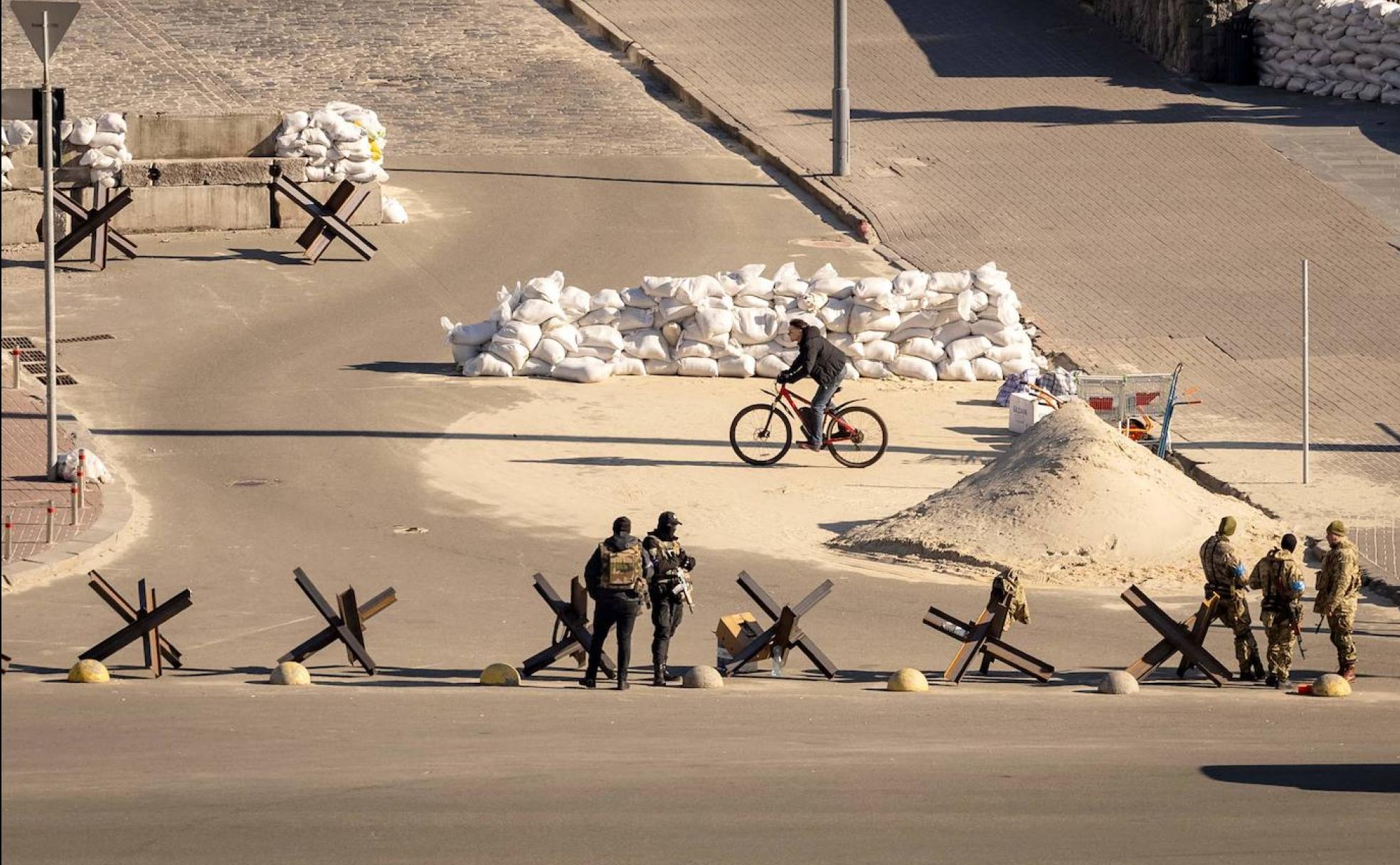  Un ciclista pasa junto a los militares ucranianos que hacen guardia en un puesto de control en el centro de Kiev.