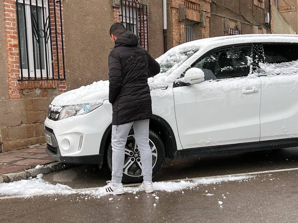 Un vecino de la Avenida de La Naval (Reinosa) retira la nieve acumulada sobre su coche.