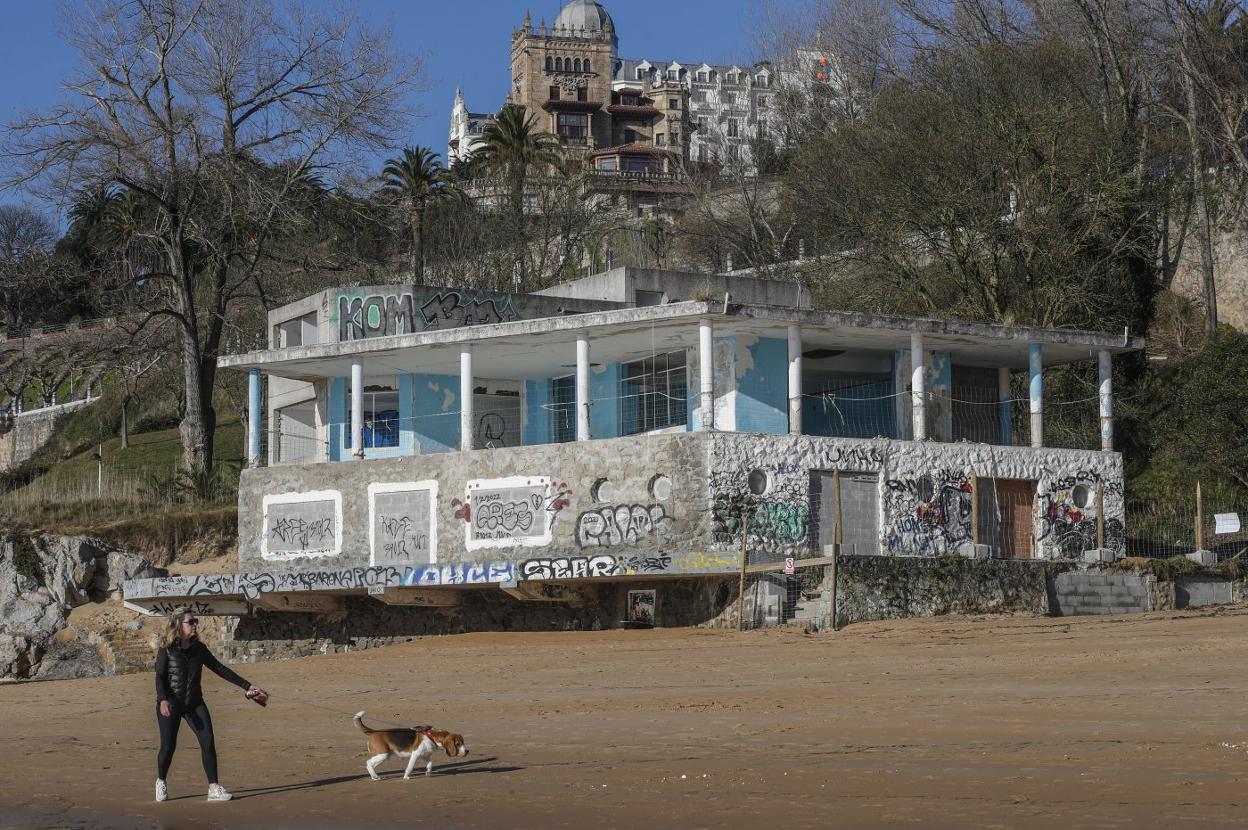 Una mujer pasea junto a su perro por la playa de Los Peligros, con el edificio de La Horadada de fondo.