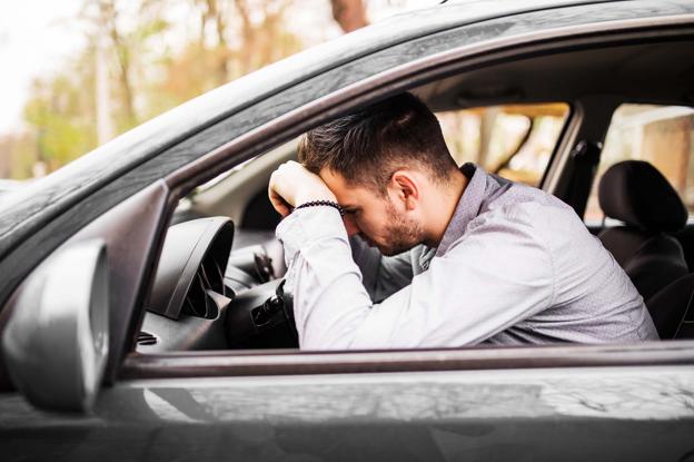 Joven abatido sobre el volante de su coche.