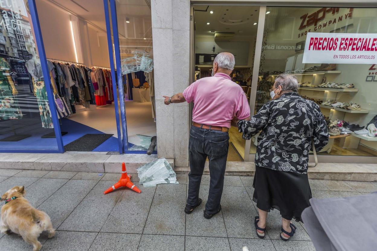 Un hombre señala el escaparate reventado de uno de los comercios. 