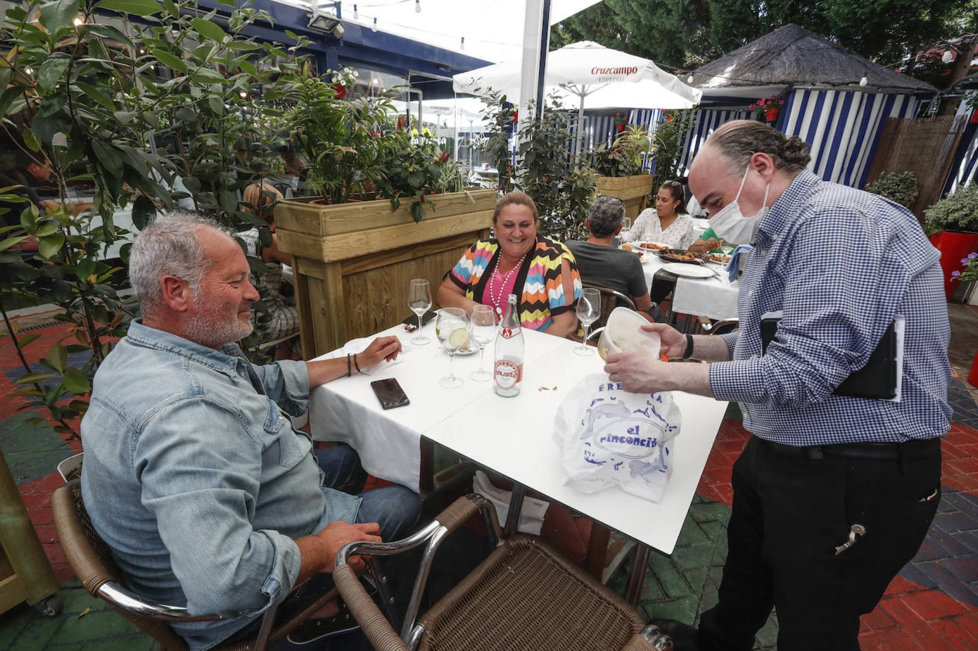 El encargado de la Taberna La Prensa entrega a Juan Carlos de José, cliente, un táper con la comida que les sobró este jueves.