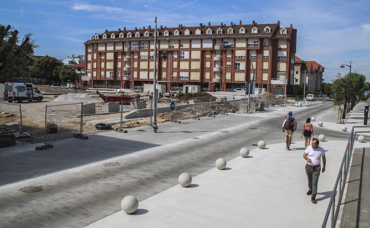 Algunas personas pasean por la recién reformada calle Peñas Blancas junto a las obras en ejecución de la plaza de Somo.