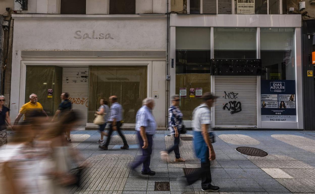 Paseantes por la calle San Francisco, en Santander, ante dos locales con la persiana echada.