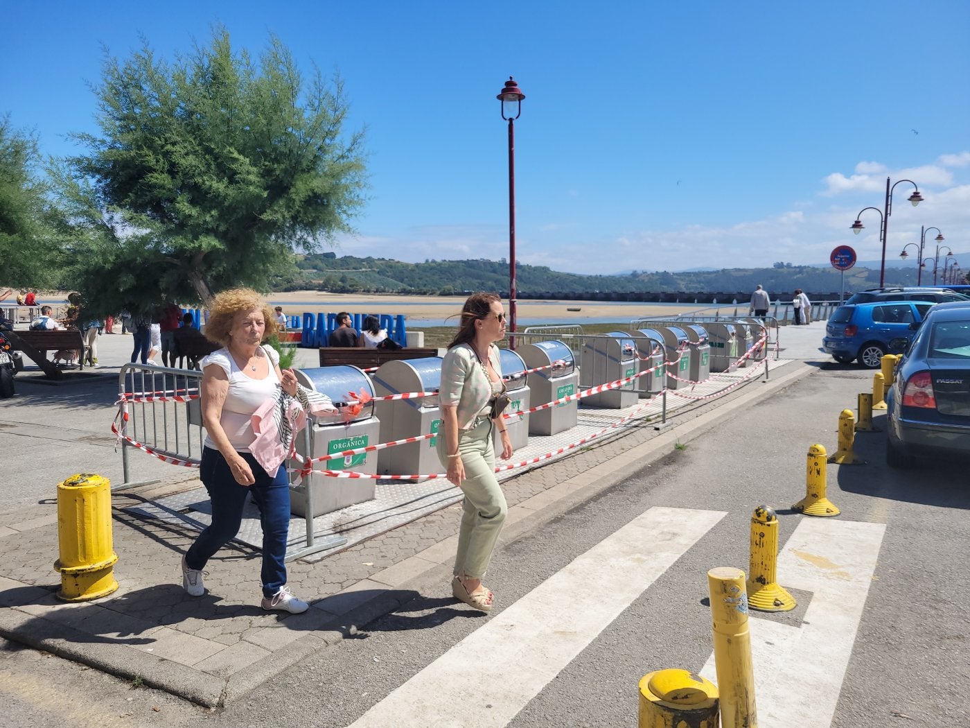 Dos mujeres cruzan un paso de cebra, junto a la hilera de contenedores soterrados. 