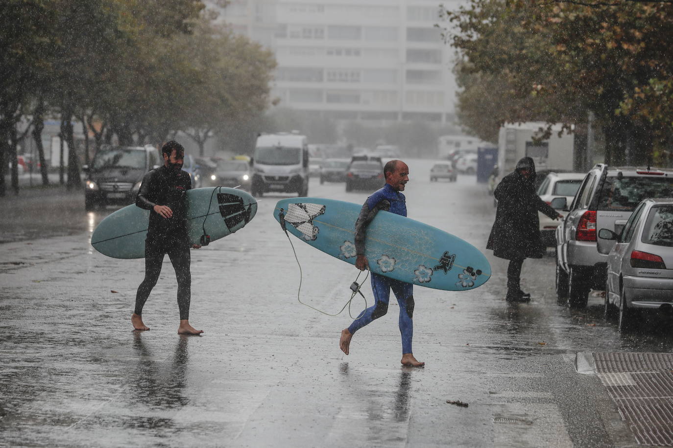 Dos surfistas cruzan en medio del temporal por las calles de Santander.