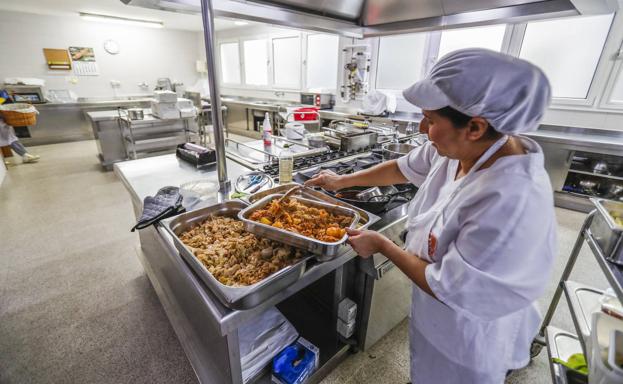 Una trabajadora, en la cocina, prepara las bandejas para la comida.