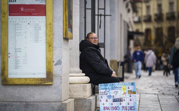 Jesús Ruiz sentado a la puerta del Teatro Real con la imagen de los números con los que participa. 