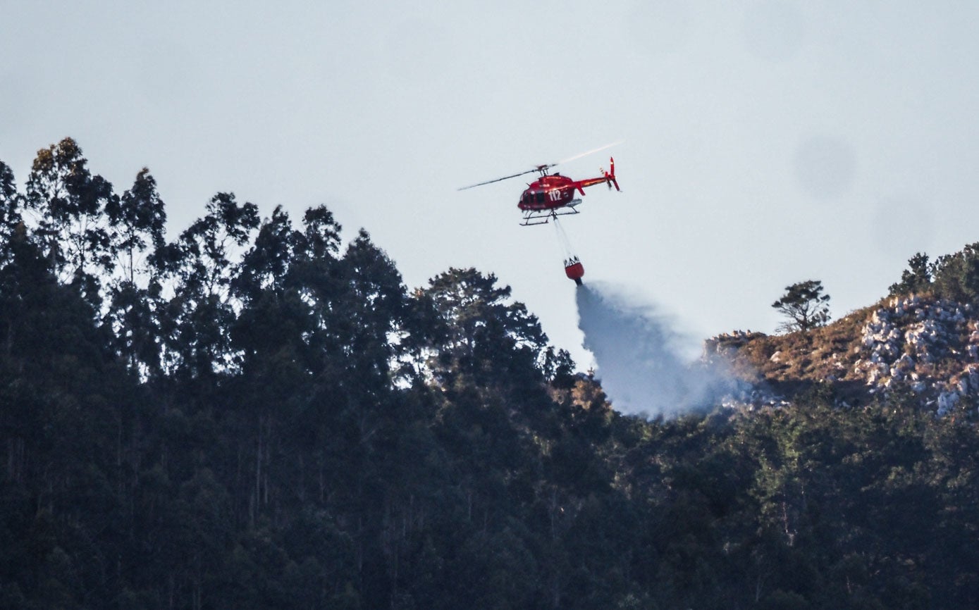 El helicóptero del 112 suelta agua sobre las zonas quemadas para apagar el fuego