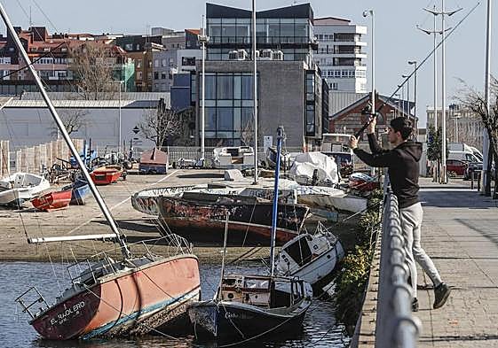 Un chico pesca junto a varios barcos abandonados en el barrio Pesquero.