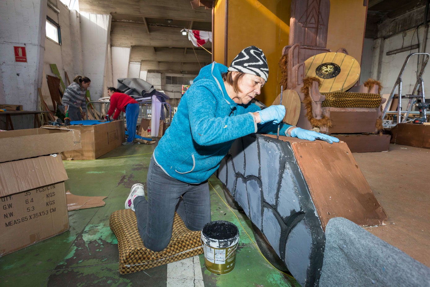 Una mujer utiliza pintura para decorar la estructura de la carroza con la que desfilarán mañana sábado.