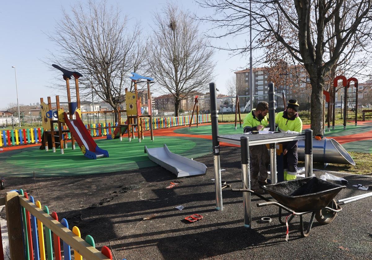 Dos operarios instalan juegos en el renovado parque infantil de Campuzano.