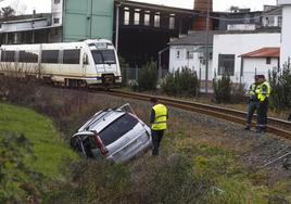 Agentes de la Guardia Civil inspeccionan el turismo siniestrado, que quedó recostado sobre la cuneta izquierda, con el tren detenido al fondo.