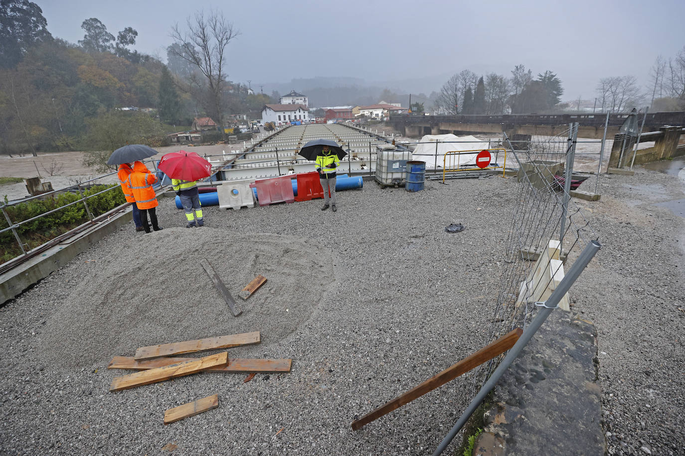 Varios trabajadores se refugian de la lluvia con paraguas con la carretera cerrada al tráfico por la construcción del puente. 