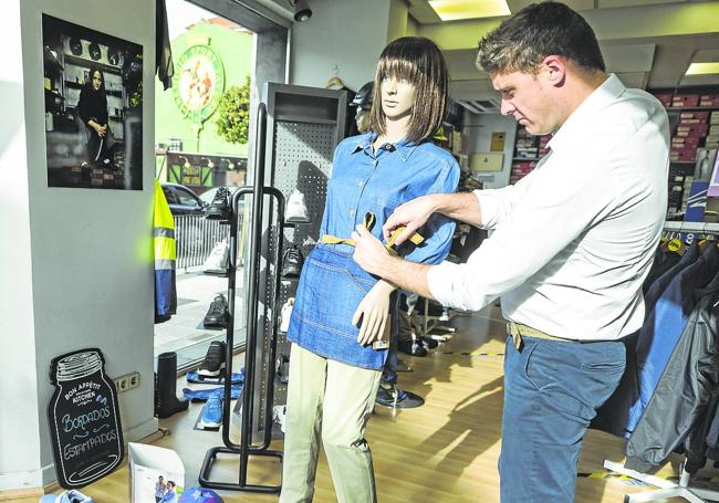 Óscar Ojea, empleado, con zapatillas homologadas, pantalón chino azul marino y camisa elástica de manga larga, prepara el maniquí con camisa y delantal confeccionados en tejidos 'denim'.