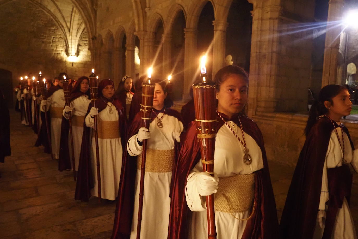 Mujeres vestidas de nazareno cruzan el claustro de la Catedral, iluminado por antorchas