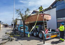 Dos operarios gestionan la retirada de uno de los barcos abandonados en el barrio Pesquero.