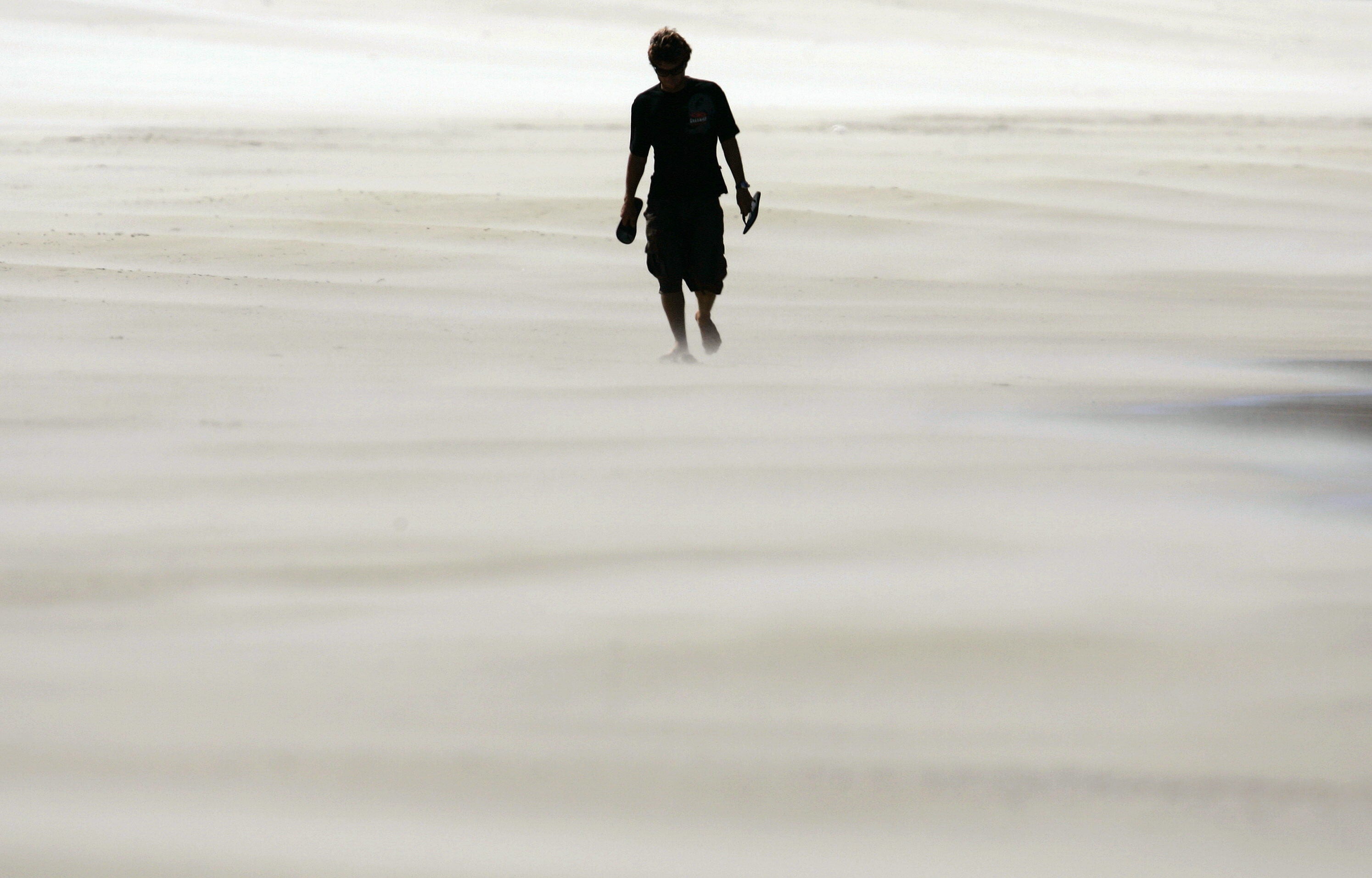 Un hombre pasea por la playa envuelto en un remolino de arena.