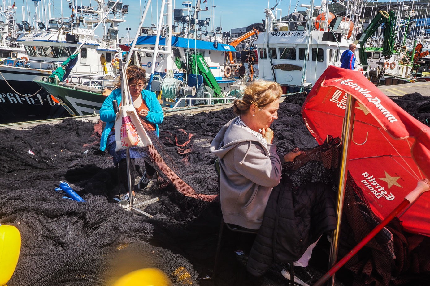 Mientas los marineros desembarcan los bocartes, las rederas reparan las redes a pie de puerto.