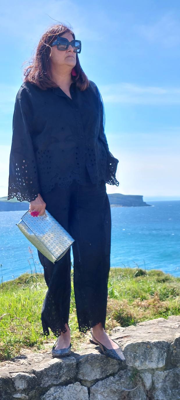 Traje negro con zapatos planos, bolso plateado y gafas negras.