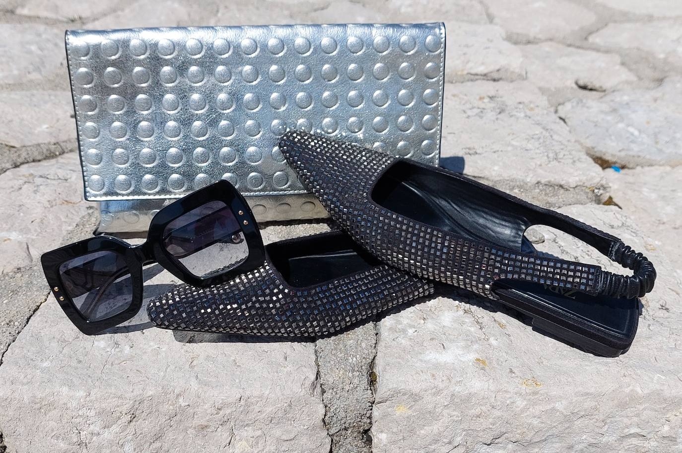 Zapatos planos, clutch plateado y gafas negras.