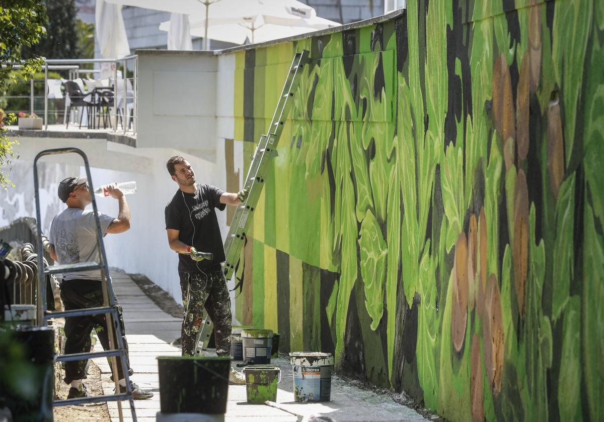 Néstor del Barrio, director creativo de UUUUU.estudio, y un colaborador trabajan en el mural de la senda de Mataleñas.