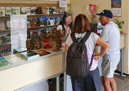 Una técnico de la oficina de turismo atiende a dos visitantes en Comillas.