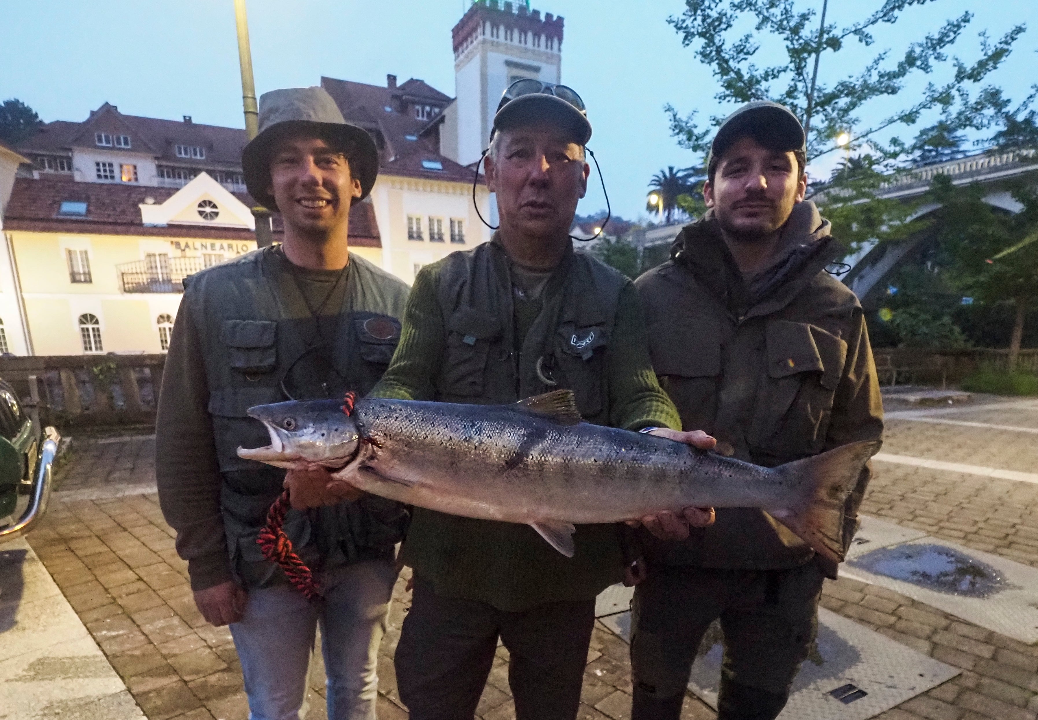 El pescador asturiano junto a sus hijos, Saúl y Miguel, con el preciado trofeo ante el Balneario de Puente Viesgo.