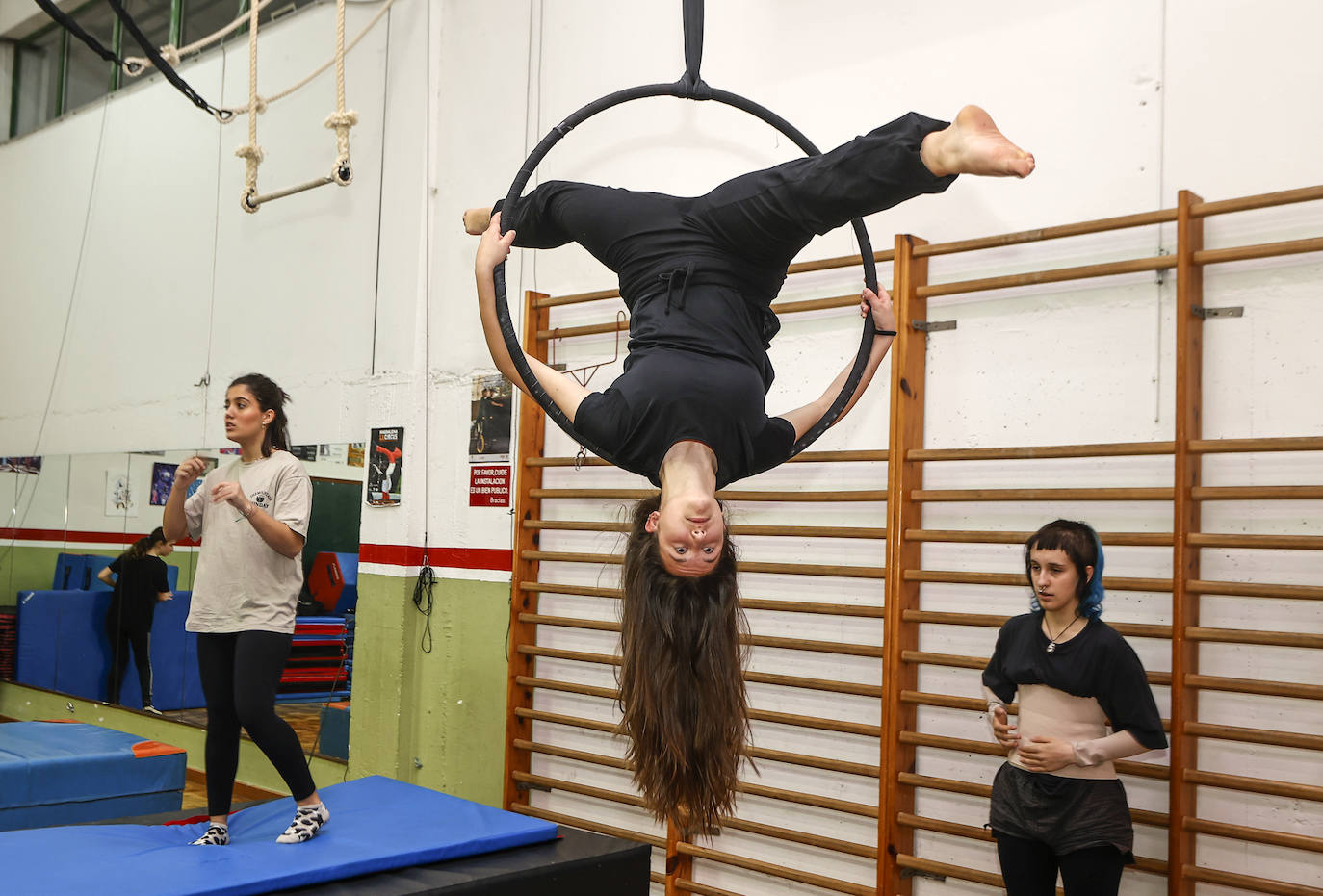 Una alumna realiza acrobacias en el trapecio, ante la mirada y el apoyo de sus compañeras de clase. 