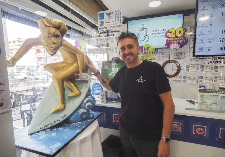 Marcos Sánchez, propietario del negocio, junto a la escultura del surfista de oro que colocaron hace unos días y que creen que ha sido clave para repartir tanta suerte.