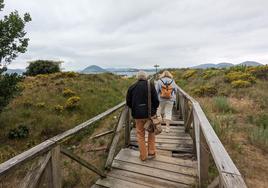 Dos personas caminan sobre la pasarela tratando de evitar las zonas desprovistas de tablas que representan un peligro en su tránsito hacia el embarque de la lancha a Santoña.