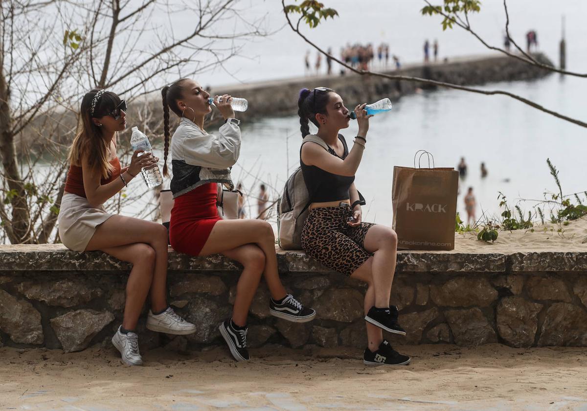 Tres jóvenes se refrescan y protegen del sol en la Playa de los Bikinis.