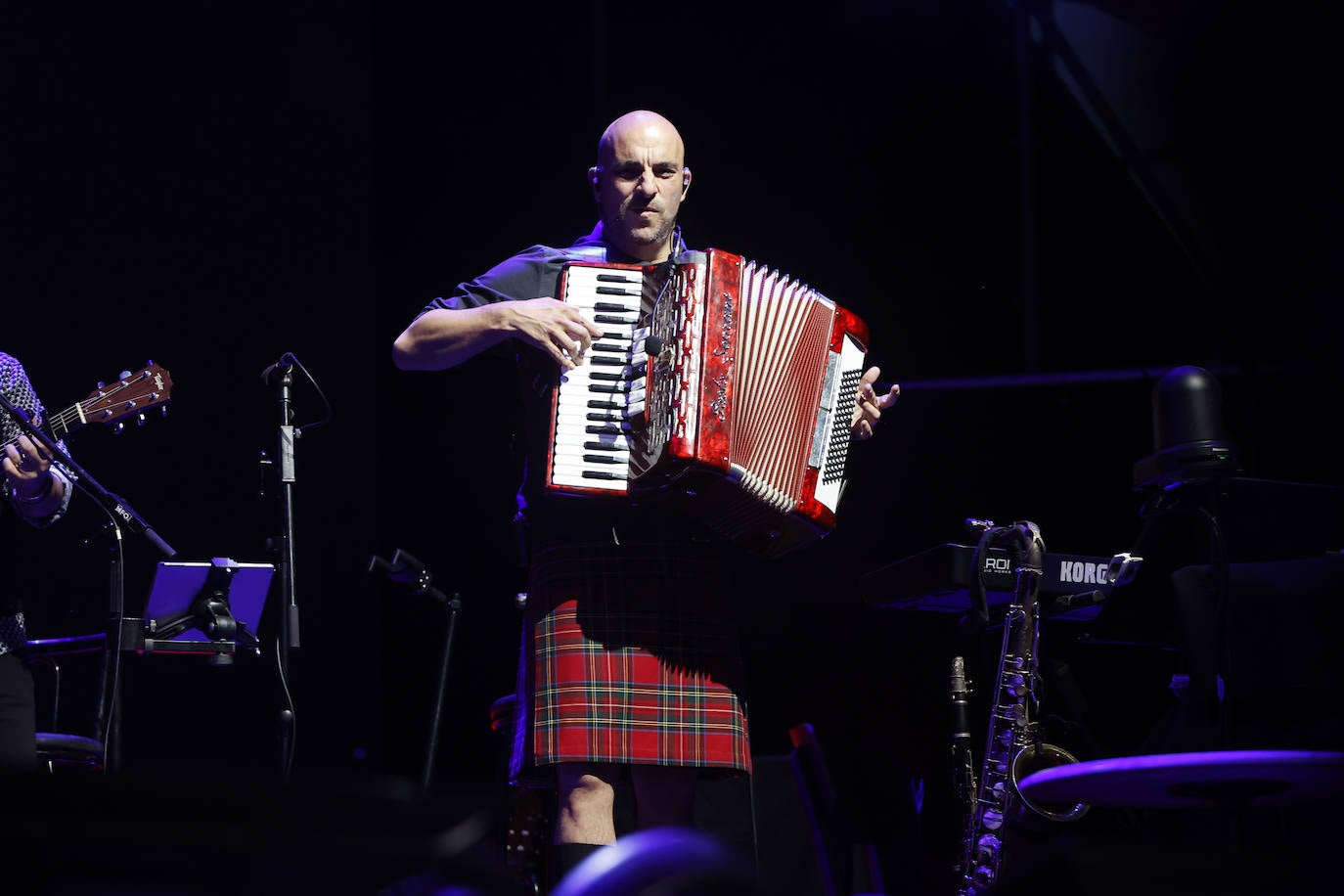 El músico Josemi Sagaste acompaña a Sabina tocando el saxofón y el acordeón, y luciendo como suele hacer una falda escocesa.