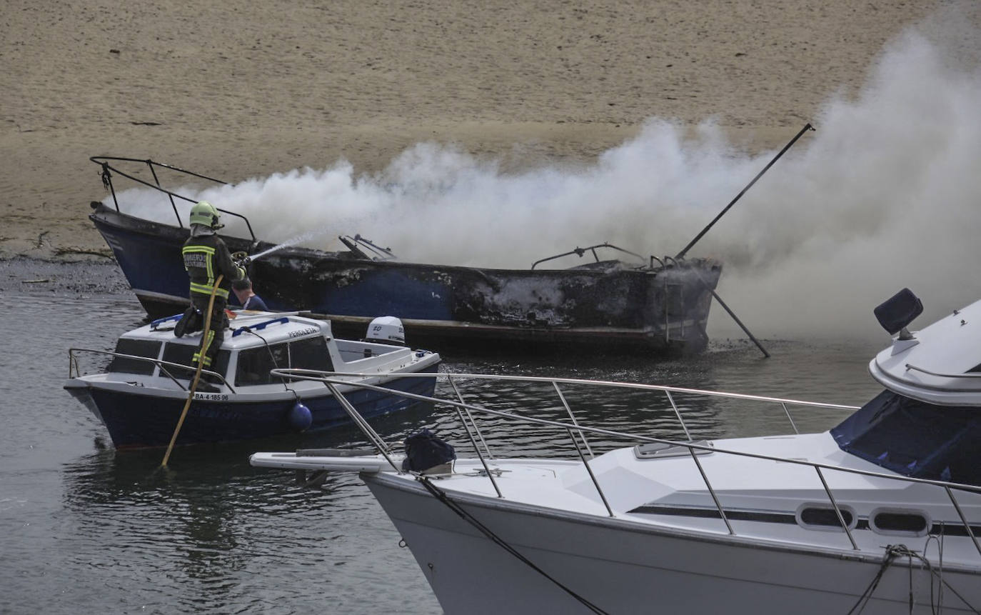 El bombero del Parque de Emergencias de Valdáliga enchufa agua sobre el barco calcinado.