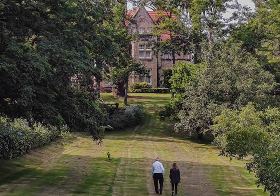 El propietario de la finca, Manolo Cardeñoso, y la periodista Mariana Cores, paseando por el jardín, con la casa al fondo