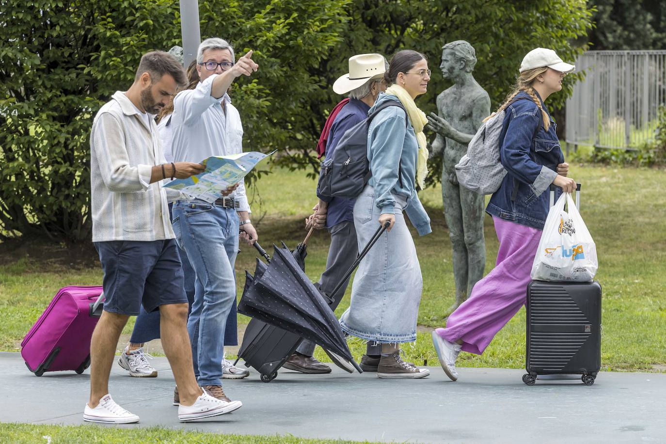 Un par de turistas ojea un mapa mientras, al fondo, tres mujeres cargadas con maletas se desplazan por la capital cántabra.