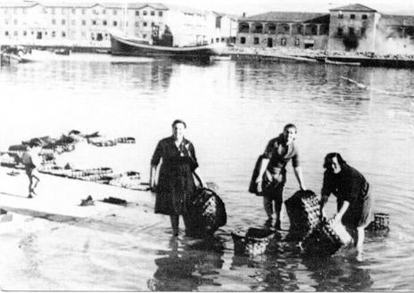 Imagen secundaria 1 - Mujeres lavando cajas en la rampa de las bodegas, frente al Barrio Pesquero y pesqueros atracados en Puertochico, circa 1940. 