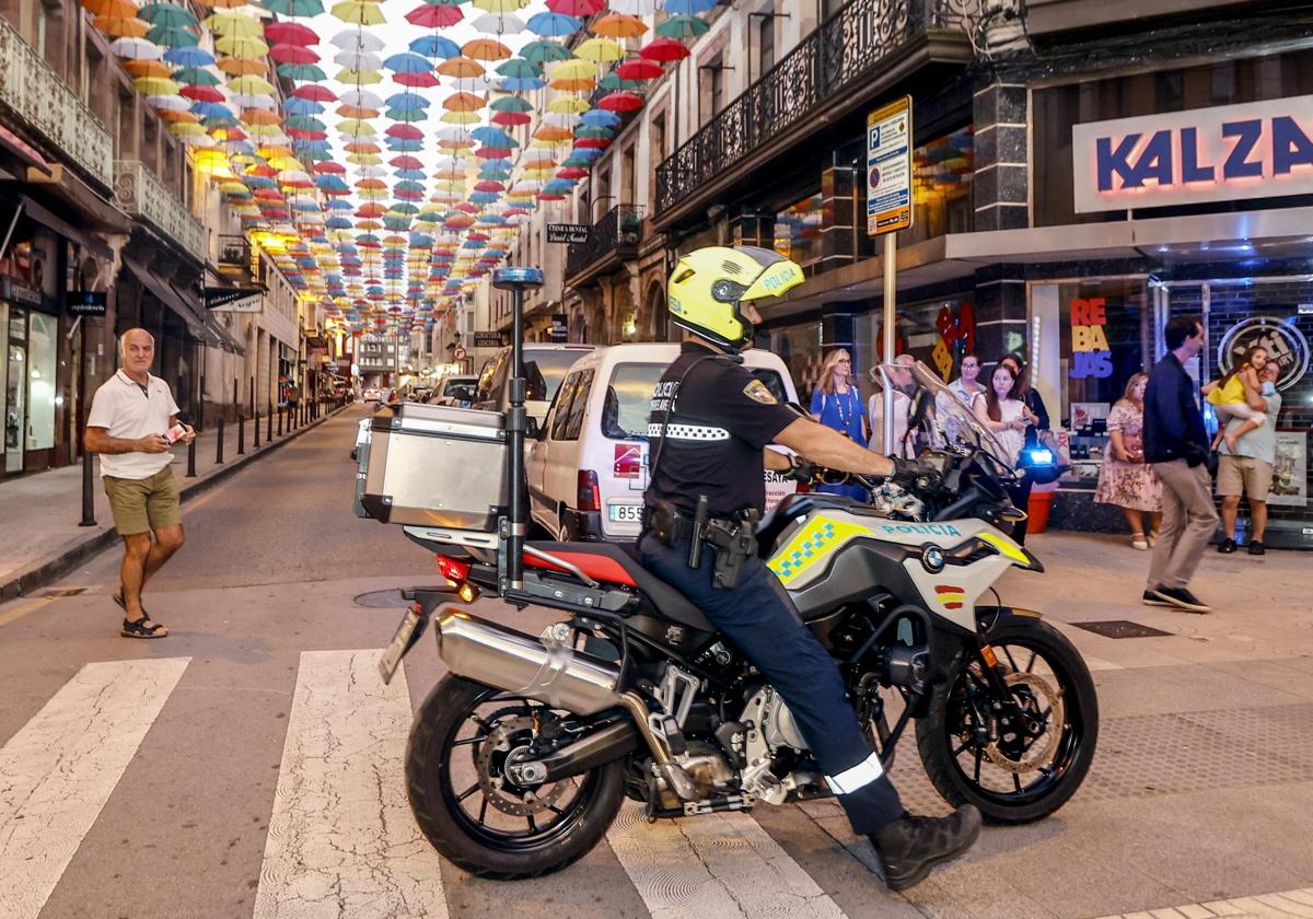 Un agente patrulla con su moto en la calle Joaquín Hoyos, adornada con paraguas durante las fiestas de la ciudad.