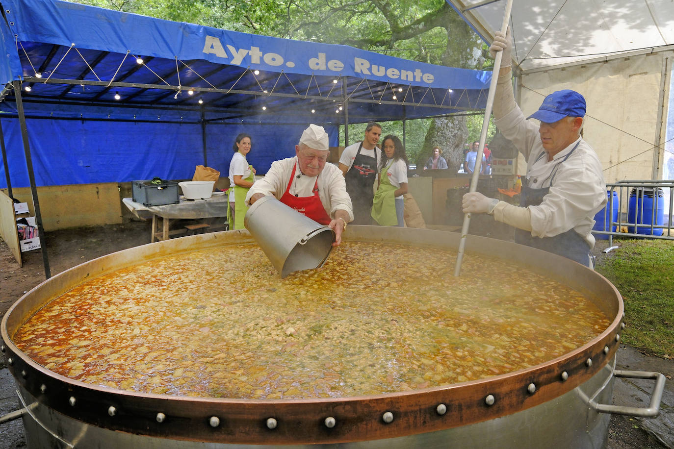 El cocinero vierte los ingredientes mientras otro revuelve el cocido