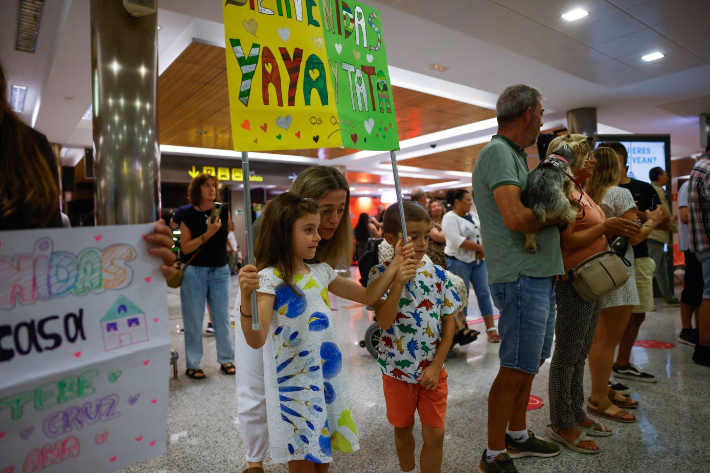 Dos hermanos recibieron a su abuela en el Seve Ballesteros con pancartas de bienvenida.