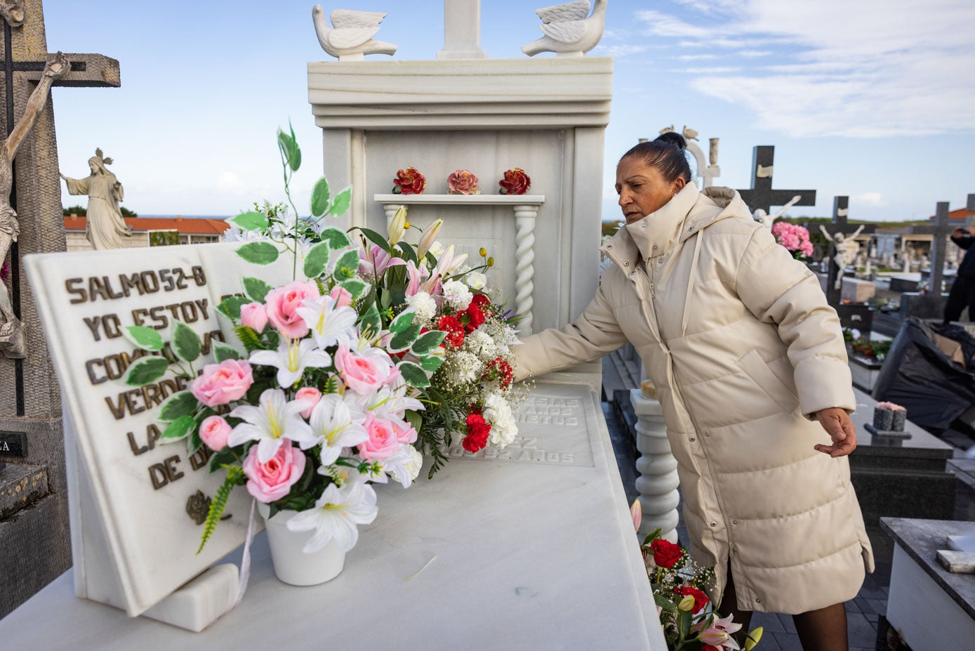 Una mujer coloca flores sobre una tumba.