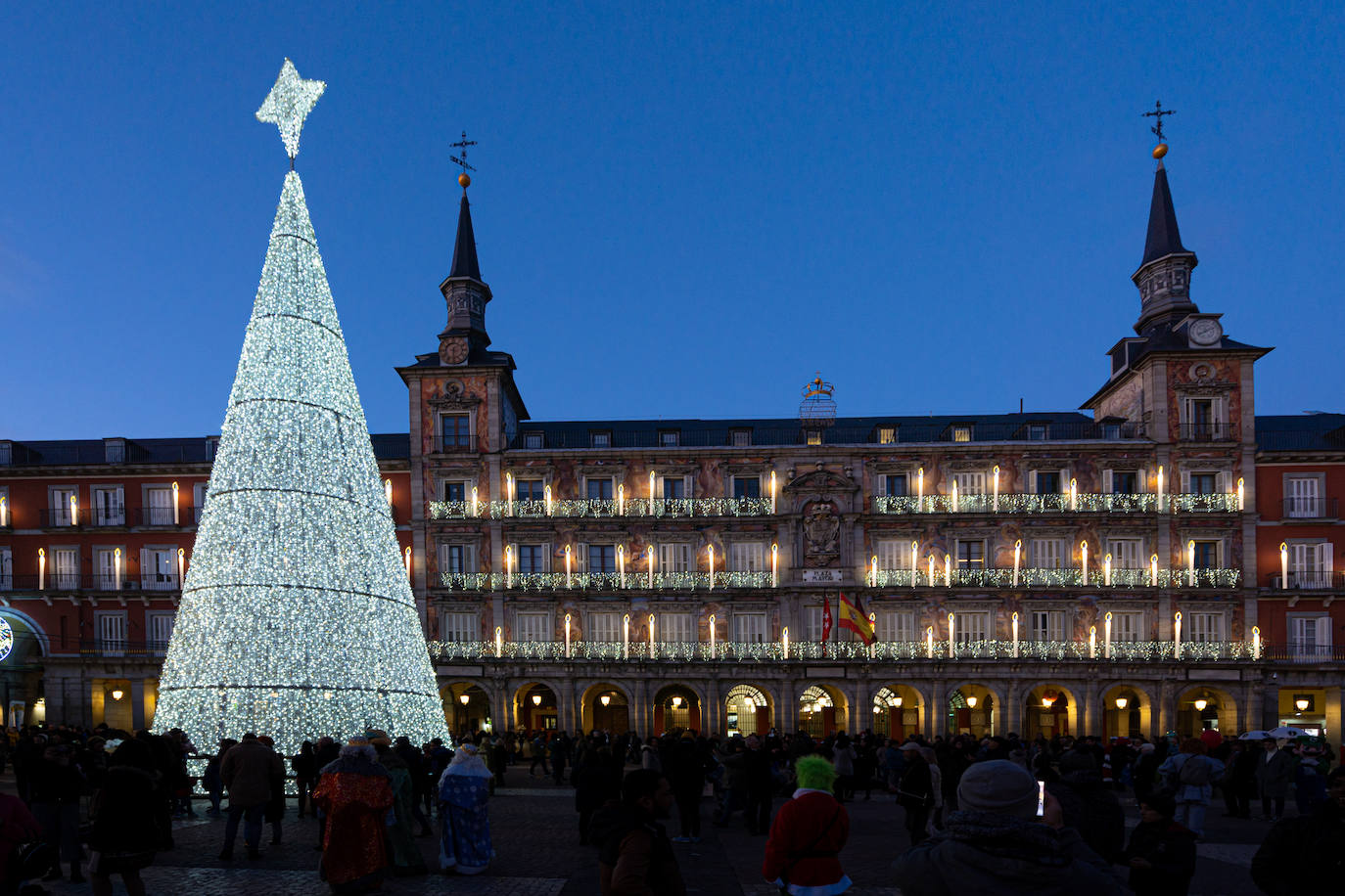 El viernes 24 de noviembre marca el esperado inicio del Mercado de Navidad en la Plaza Mayor de Madrid, un evento que transforma este emblemático enclave en un remanso de alegría, paz y amor. Las casetas de color rojo y tejados a dos aguas destacan cada años con sus mejores galas, aguardando la llegada de ciudadanos y turistas ansiosos por explorar los 104 puestos. En este rincón tan especial de la ciudad, además de disfrutar del tradicional mercadillo navideño que ha sido una tradición anual, se puede admirar un imponente árbol de Navidad. Aunque no es de origen natural, su estructura metálica se erige majestuosamente, adornada por un sinfín de luces que culminan en una estrella resplandeciente. Este árbol, que se alza aproximadamente a 16 metros de altura, se convierte en un faro luminoso que ilumina la temporada festiva en Madrid, añadiendo un toque mágico a la experiencia navideña en la Plaza Mayor.