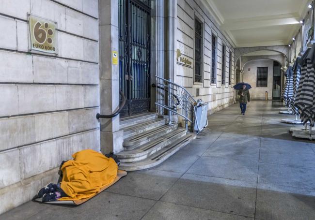 Una persona sintecho dormía sobre unos cartones y bajo una manta, en la noche del miércoles, en los soportales de la plaza Porticada de Santander.