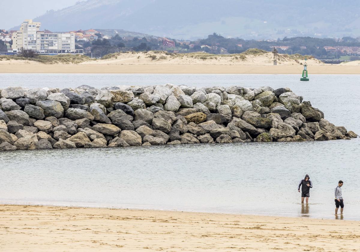 Imagen de dos paseantes junto al espigón de la playa de La Magdalena.