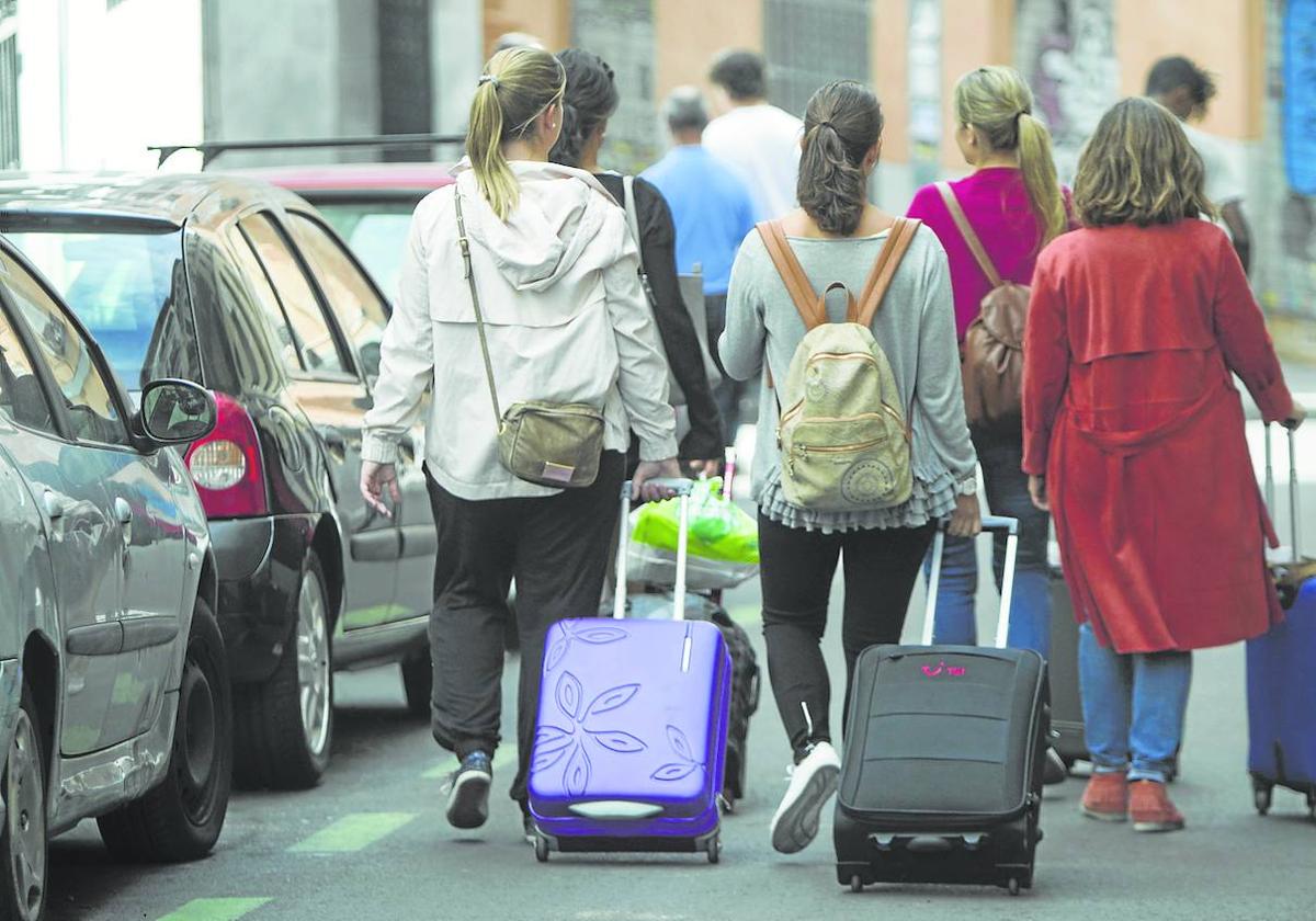 Un grupo de turistas camina por la calle tirando de sus maletas.