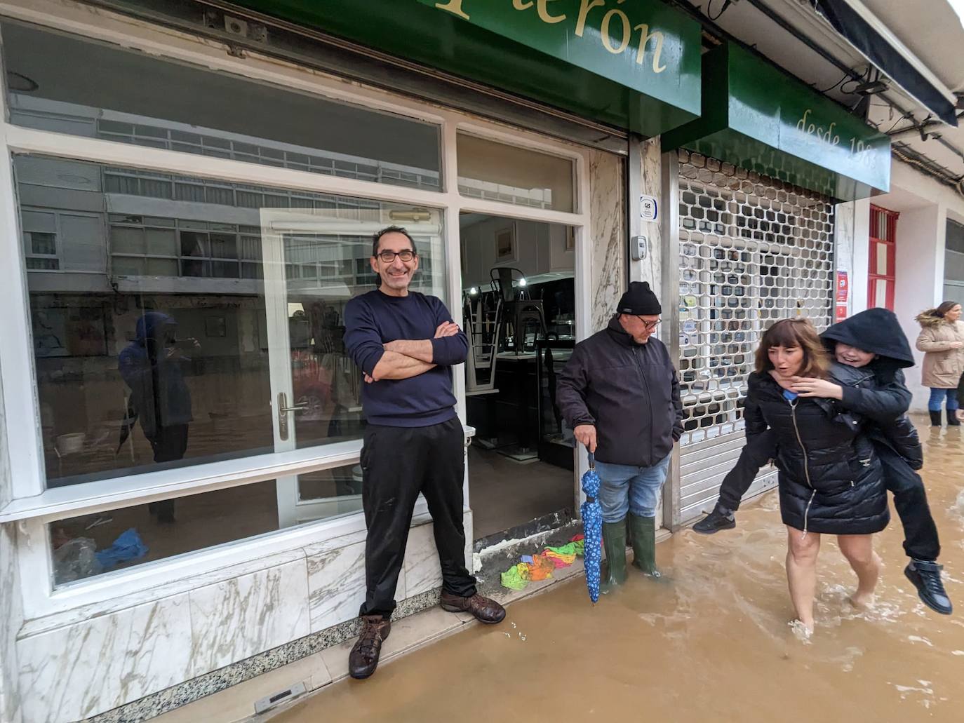 En la calle Martínez Balaguer de Laredo, a la altura del bar Boquerón, llevan desde ayer bajo el agua. Una madre descalza carga con su hijo a la espalda para salir del edificio.