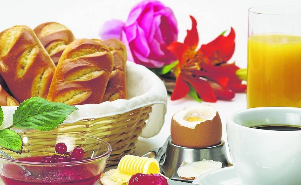 Desayuno a base de zumo de naranja, café, huevo duro y panecillos con mermelada de grosella. 