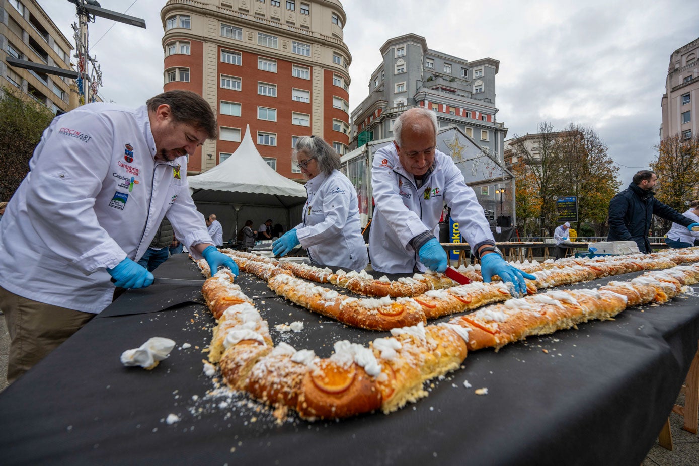 El roscón sobre las mesas en torno a la plaza es cortado por dos voluntarios.