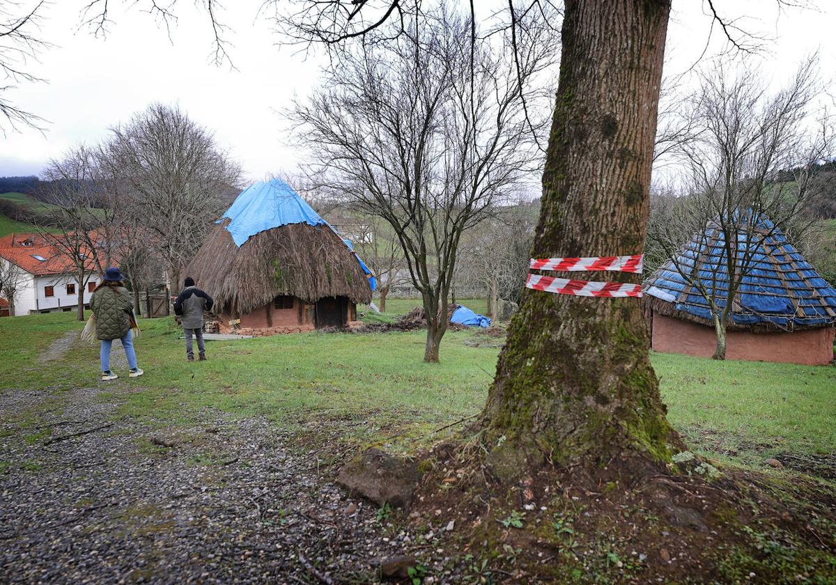 Dos visitantes caminan entre las cabañas cubiertas con plástico azul del Poblado Cántabro.